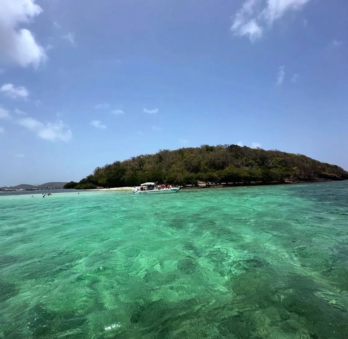 Îlet vu depuis la mer avec eau verte, ciel bleu et bateau au fond